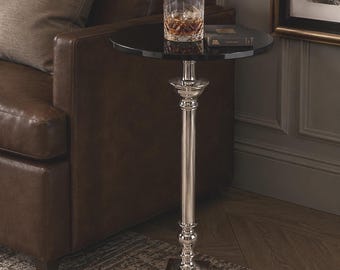 Può includere: Tavolino con piano nero e base argentata ornata. Un bicchiere di liquido color ambra con ghiaccio è appoggiato sul tavolo. Il tavolo è accanto a un divano in pelle marrone.
