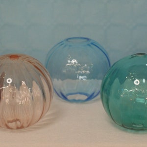 May include: Five glass balls in various colours, including purple, blue, pink, and green. The balls are round and have a smooth, shiny surface.