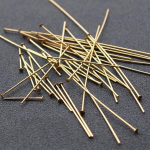 Può includere: Un mucchio di spilli con testa dorati, utilizzati per la creazione di gioielli e l'artigianato.