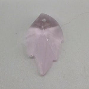 May include: A pale pink, leaf-shaped crystal pendant with a small hole at the top for stringing. The crystal has a faceted design, catching light and creating a shimmering effect. The pendant is a delicate, nature-inspired accessory.