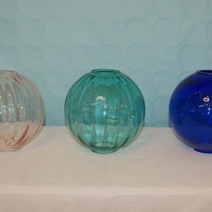 May include: Three glass globe-shaped vases, one pink, one teal, and one blue.