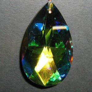 May include: A faceted, teardrop-shaped crystal pendant. The pendant has a complex, multi-colored appearance with hues of blue, green, and yellow. It is suspended by a thin, reddish-brown cord, suggesting it is designed to be worn as jewelry.