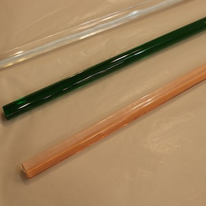 Puede incluir: Tres varillas de vidrio, una transparente, una verde y una rosa.