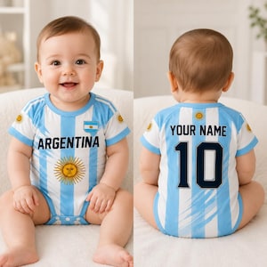 Puede incluir: Un body para bebé con el diseño de la selección nacional de fútbol de Argentina con rayas verticales azul claro y blancas. El frente muestra la palabra ARGENTINA y un emblema de sol. La parte posterior muestra el texto YOUR NAME y el número 10.