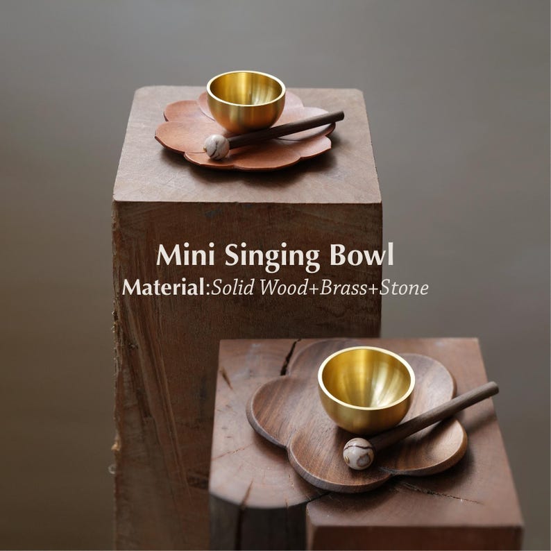May include: A mini singing bowl set made of solid wood, brass, and stone. The set includes a small gold-colored bowl, a wooden mallet with a stone head, and a wooden flower-shaped base. The text "Mini Singing Bowl" and material details are visible.