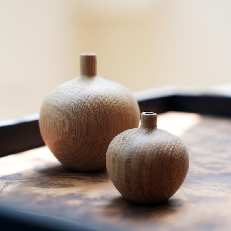 Puede incluir: Dos jarrones de madera con un acabado natural de vetas. Los jarrones son esf&eacute;ricos con un cuello estrecho. Un jarr&oacute;n es m&aacute;s grande que el otro. Los jarrones se exhiben sobre una superficie de madera oscura.