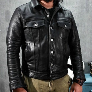 May include: A black leather jacket with a button-up front and two flap pockets. The jacket has a classic denim jacket style.