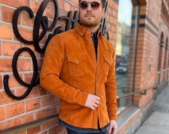 May include: A man wearing a brown suede shirt with a button-down collar and a pair of blue jeans. He is wearing sunglasses and has a beard.