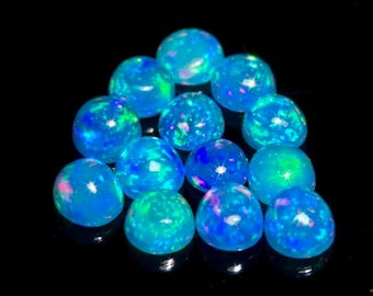 May include: A collection of round, cabochon-cut opals featuring a vibrant blue base color with internal flashes of green and pink light. Each gemstone has a smooth, polished, domed surface that reflects light, creating bright, sparkling highlights.