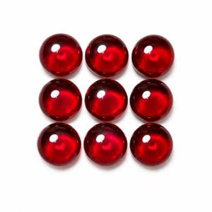 May include: Nine circular, deep red glass cabochons arranged in a three-by-three grid. Each piece features a smooth, domed surface with a reflective finish and a bright white light reflection, showcasing a translucent, vibrant crimson color throughout.