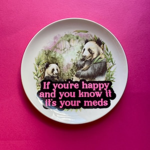 May include: A white ceramic plate featuring a detailed illustration of two pandas in a bamboo forest. Overlaid on the lower portion is a black speech bubble shape containing the bright pink text: If you're happy and you know it it's your meds.