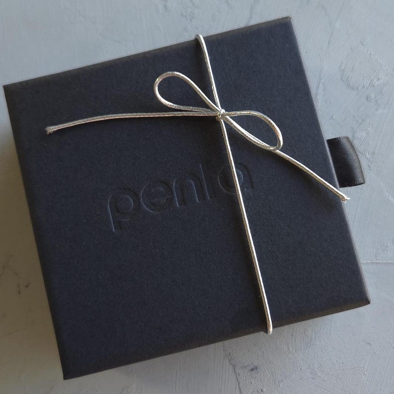 May include: A black square gift box tied with a silver string and bow. The box has the word "penlo" embossed on the top. A black ribbon is attached to the side of the box.