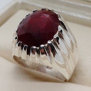 May include: A silver ring with a large, oval-shaped ruby gemstone. The ring has a textured band.