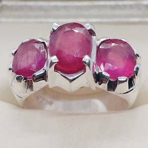 May include: A silver ring with three pink ruby stones set in the center.