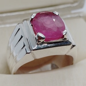 Può includere: Un anello d'argento con una pietra ovale rosa incastonata in una lunetta quadrata. L'anello ha una fascia testurizzata.