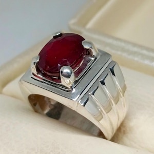May include: A silver ring featuring a large, oval-shaped ruby gemstone. The ring has a simple, elegant design with a smooth band.