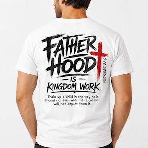 Peut inclure: Un t-shirt blanc à manches courtes avec le texte noir FATHERHOOD IS KINGDOM WORK, une croix rouge et le texte PROVERBS 22:6. En dessous, un texte noir plus petit indique : Train up a child in the way he is should go; even when he is old he will not depart from it.