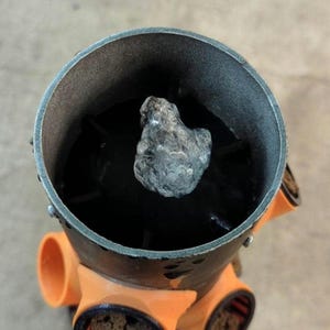 K&ouml;nnte beinhalten: Nahaufnahme eines Metallobjekts mit dunklem Innenraum und einem grauen, strukturierten Stein im Inneren. Das Objekt hat orangefarbene Aufs&auml;tze an der Unterseite.