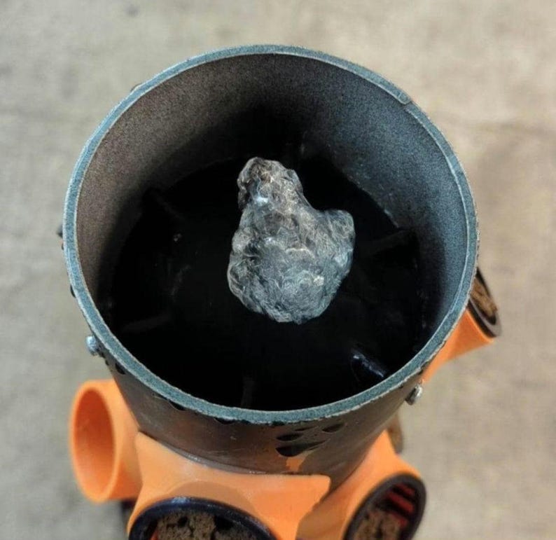 K&ouml;nnte beinhalten: Nahaufnahme eines Metallobjekts mit dunklem Innenraum und einem grauen, strukturierten Stein im Inneren. Das Objekt hat orangefarbene Aufs&auml;tze an der Unterseite.