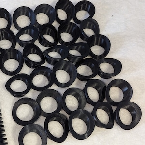 May include: A collection of black plastic rings, likely for crafts or DIY projects. The rings are stacked and arranged in a triangular shape.