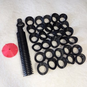 Op de afbeelding: Een set zwarte plastic hydroponische netpotten met een rode irrigatie-emitter en een zwarte irrigatieslang. De netpotten zijn in een halve cirkel gerangschikt.