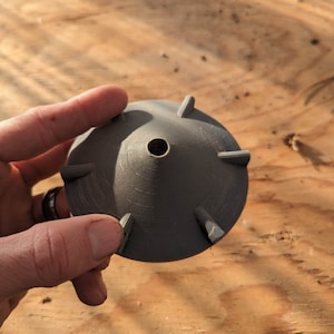 Op de afbeelding: Een grijze plastic 3D-geprinte kegel met een gat in het midden en vijf punten rond de rand.