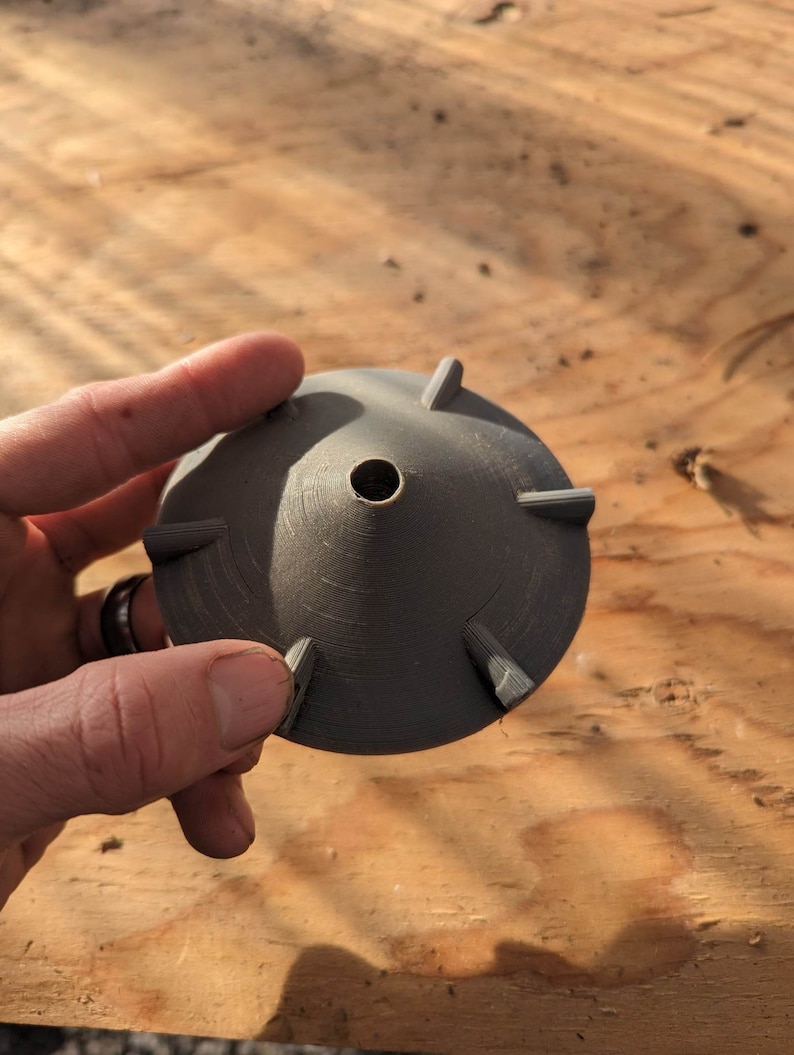 Op de afbeelding: Een grijze plastic 3D-geprinte kegel met een gat in het midden en vijf punten rond de rand.