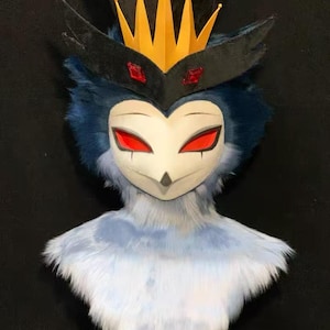 May include: A bust of a bird-like character featuring a white face with red eyes, dark blue fur, and a tall black top hat. A yellow crown sits on the front of the hat, accented by two red rectangular gems on a black band above the eyes.