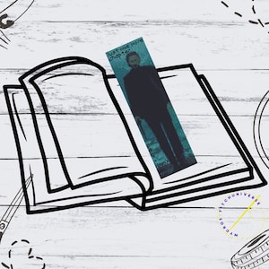 May include: A black and white illustration of an open book with a bookmark that says "Just one more chapter". The bookmark has a blue and green pixelated image of a person. The book is on a white wooden surface with sewing supplies.