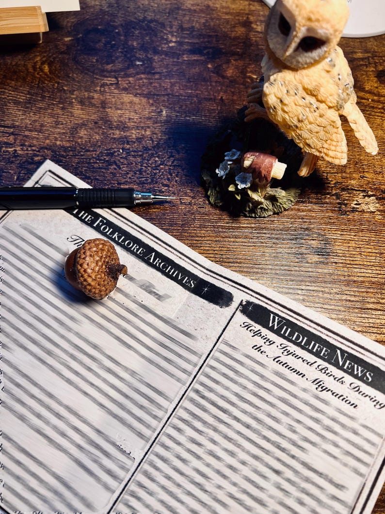 May include: A printed document titled The Folklore Archives and Wildlife News: Helping Injured Birds During the Autumn Migration, featuring a black pen, a small brown acorn, and a tan owl figurine perched on a base with small white flowers.