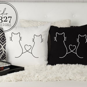 May include: Two white throw pillows with black outlines of two cats facing each other with their tails intertwined to form a heart. One pillow is white with black outlines and the other pillow is black with white outlines.