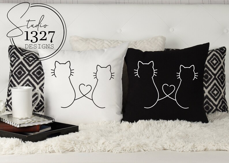 May include: Two white throw pillows with black outlines of two cats facing each other with their tails intertwined to form a heart. One pillow is white with black outlines and the other pillow is black with white outlines.