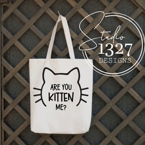 May include: White tote bag with black cat ears and the text "Are you kitten me?" printed on the front.