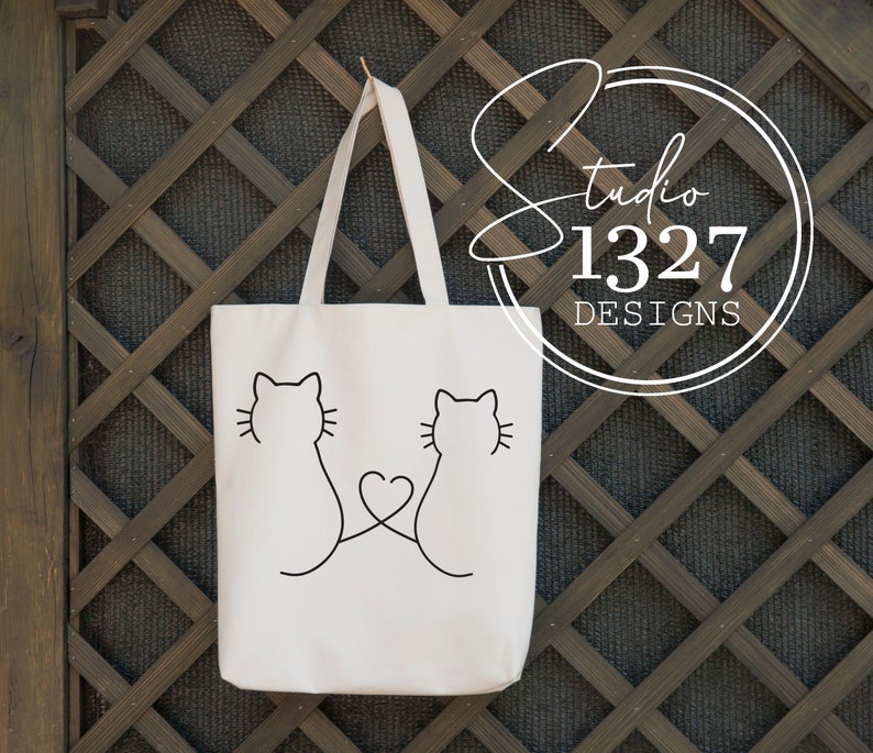 May include: White tote bag with black outline of two cats facing each other with a heart in the middle. The text "Studio 1327 Designs" is on a circle in the upper right corner.