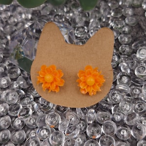 May include: A pair of orange flower-shaped stud earrings on a brown card shaped like a cat.