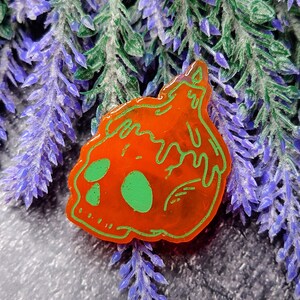 May include: Orange and green resin pin shaped like a skull with dripping paint.