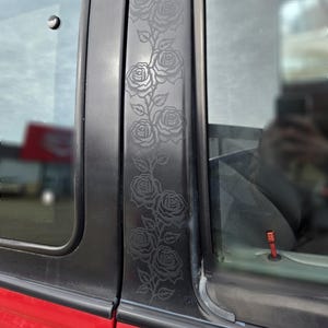 May include: A black car door with a decorative rose design etched into the window trim. The roses are arranged vertically in a vine-like pattern.