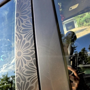 K&ouml;nnte beinhalten: Nahaufnahme eines Autot&uuml;rrahmens mit einem dekorativen Blumenmuster, das in die schwarze Zierleiste ge&auml;tzt ist. Das Design ist ein sich wiederholendes Muster stilisierter Blumen. Der angrenzende Rahmen ist einfarbig, mattschwarz.