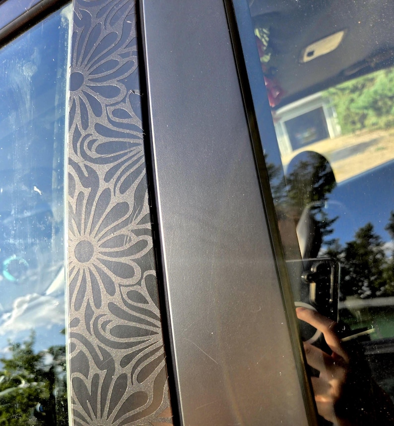 K&ouml;nnte beinhalten: Nahaufnahme eines Autot&uuml;rrahmens mit einem dekorativen Blumenmuster, das in die schwarze Zierleiste ge&auml;tzt ist. Das Design ist ein sich wiederholendes Muster stilisierter Blumen. Der angrenzende Rahmen ist einfarbig, mattschwarz.