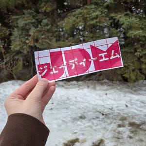 May include: A pink and white sticker with the text "JDM" and Japanese characters that read "J-Dream" on a grid background.