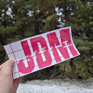 May include: A pink vinyl sticker with the word "JDM" in white letters on a white grid background.