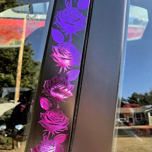 May include: Black car door trim featuring a vertical pattern of purple and pink roses. The roses, with detailed petals and green leaves, stand out against the dark backdrop. The design is repeated along the trim, creating a decorative effect.