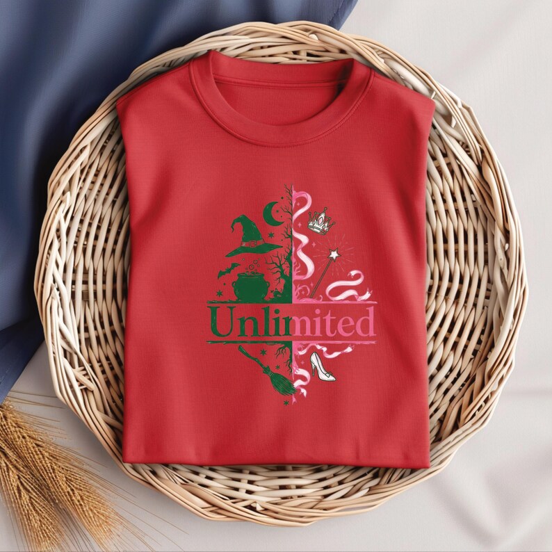 May include: A red t-shirt with a graphic design featuring witch-themed elements. The design includes a witch hat, cauldron, broom, and high heel. The word "Unlimited" is printed in green and pink.