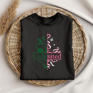 May include: Black t-shirt featuring a split design with green and pink graphics. The left side shows a witch's hat and broom, while the right side has a crown and high heel. The word "Unlimited" is printed in the center.