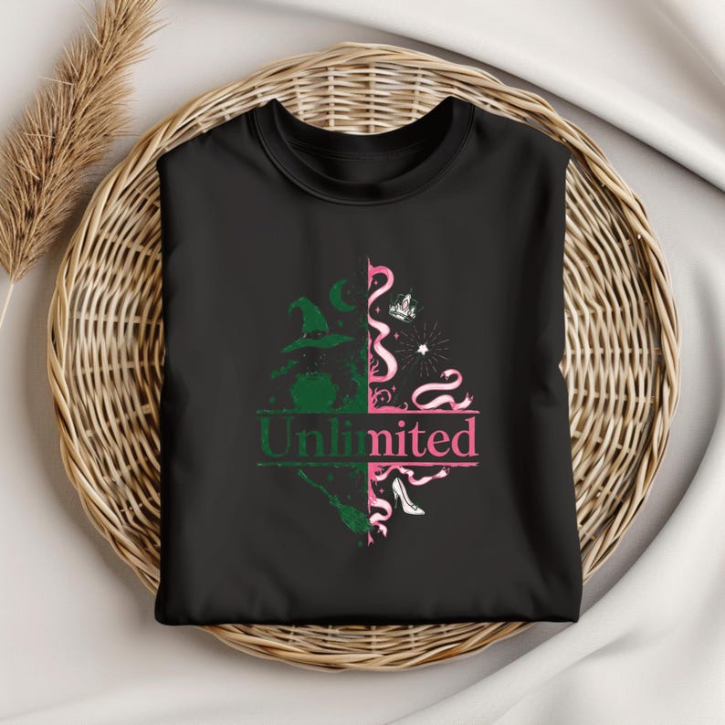 May include: Black t-shirt featuring a split design with green and pink graphics. The left side shows a witch's hat and broom, while the right side has a crown and high heel. The word "Unlimited" is printed in the center.
