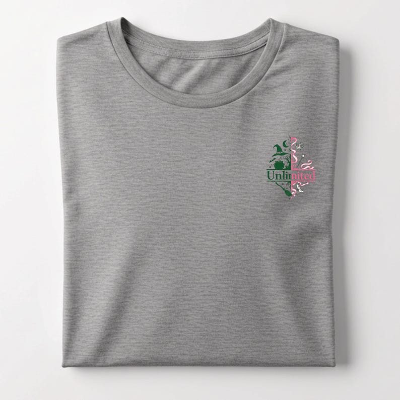 May include: A heather gray t-shirt with a crew neck. The shirt features a small graphic on the left chest with the word "Unlimited" and a design of a witch's hat, broom, and other elements in green and pink.
