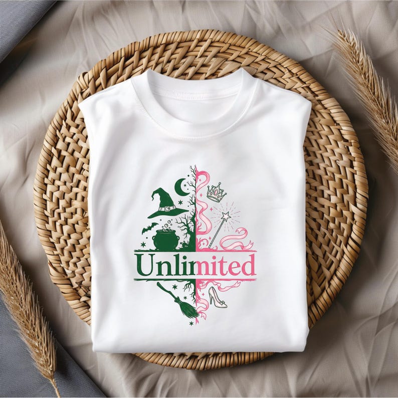 May include: White t-shirt with a split design featuring a witch-themed side with a hat, cauldron, and broom, and a princess-themed side with a crown, wand, and shoe. The word "Unlimited" is printed across the center in green and pink.