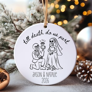 Puede incluir: Un adorno redondo de cerámica blanca con un dibujo de líneas negras de un esqueleto con esmoquin arrodillado ante un esqueleto con vestido de novia. El texto dice "till death do us part", "JASON & NATALIE" y "2026" en tinta negra.