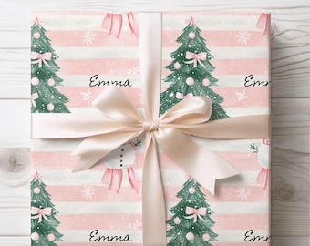 May include: A wrapped gift with a festive Christmas theme. The wrapping paper features a pattern of pink and white stripes, Christmas trees, snowmen, and snowflakes. The gift is tied with a cream-colored satin ribbon and bow. The name "Emma" is printed on the wrapping paper.