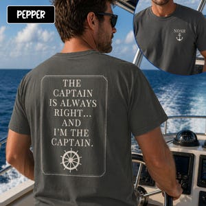 Pu&ograve; includere: T-shirt grigio scuro con la scritta "THE CAPTAIN IS ALWAYS RIGHT... AND I'M THE CAPTAIN" in un riquadro rettangolare bianco. La maglietta presenta anche una piccola grafica di un'ancora e il nome "NOAH" sul davanti. La persona indossa occhiali da sole ed &egrave; su una barca.